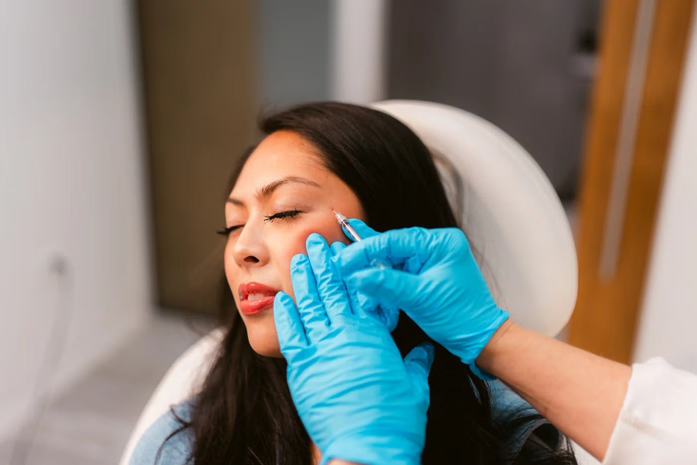 Woman receiving facial injection treatment from a professional in blue gloves.